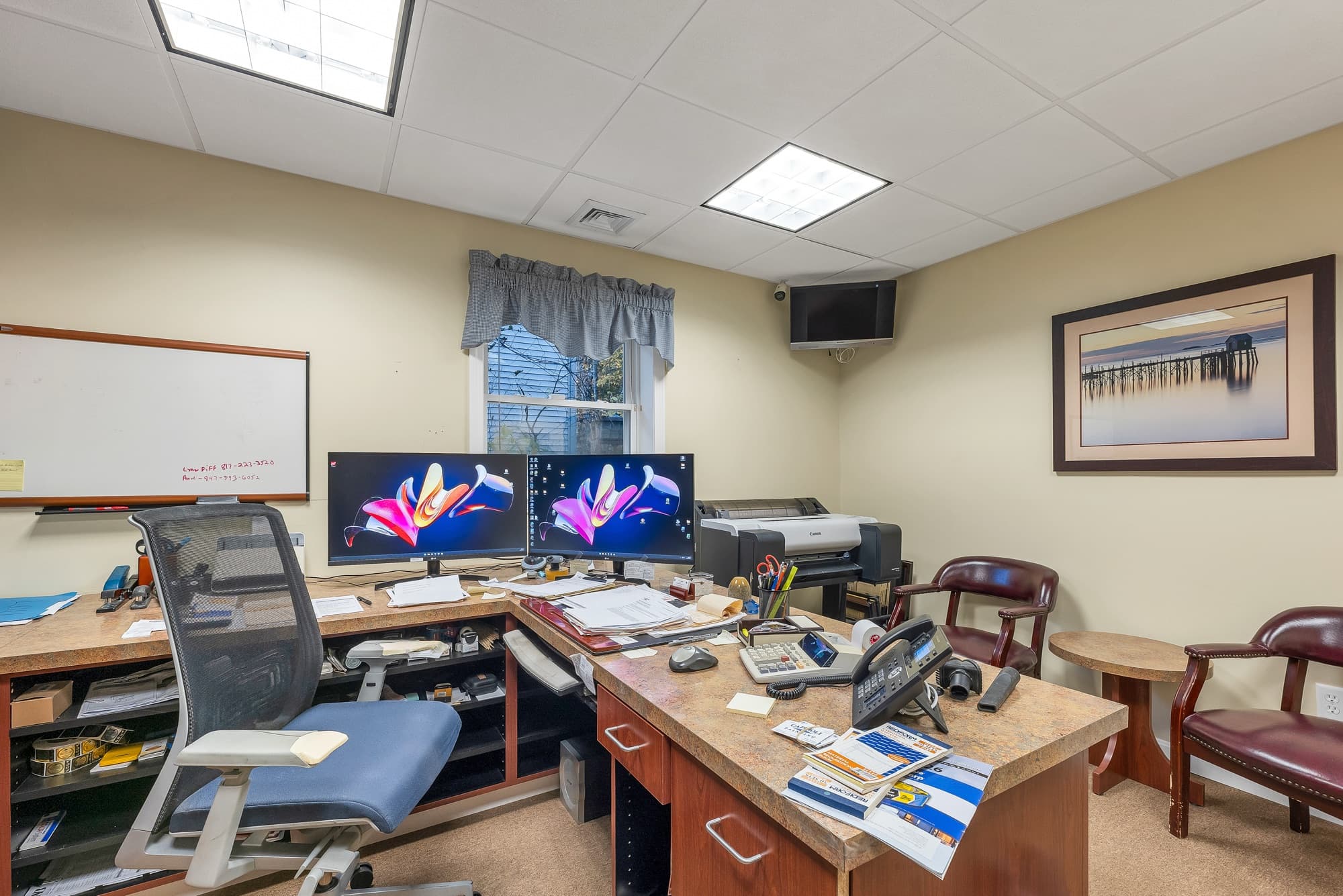 The same office from the desks, with 2 monitors, a whiteboard, and leather chairs