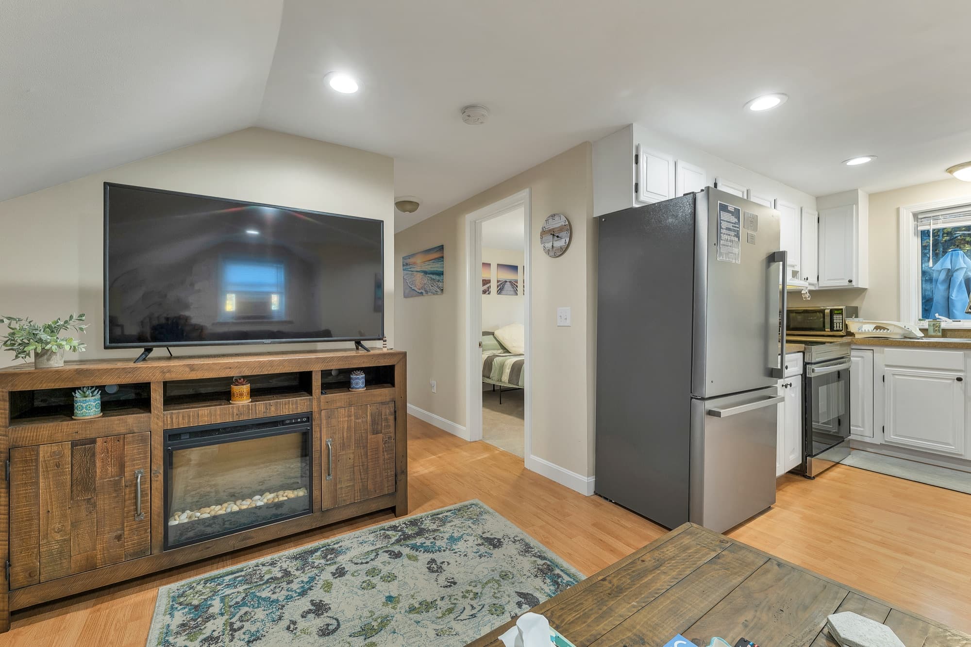 The 2-bedroom apartment's TV console with an electric fireplace, with the kitchen and a bedroom beyond
